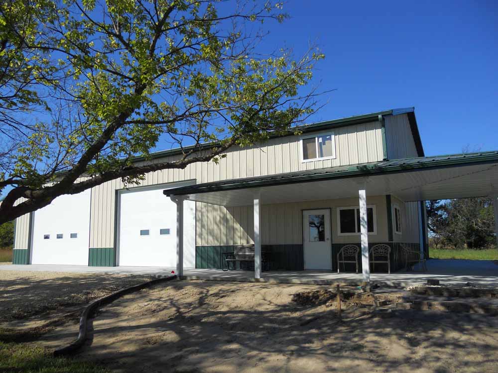Tan and green metal building with a covered porch and 2 large overhead doors