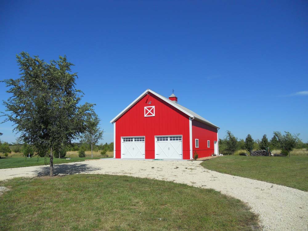 Red metal barn with two garage doors and a circle gravel drive