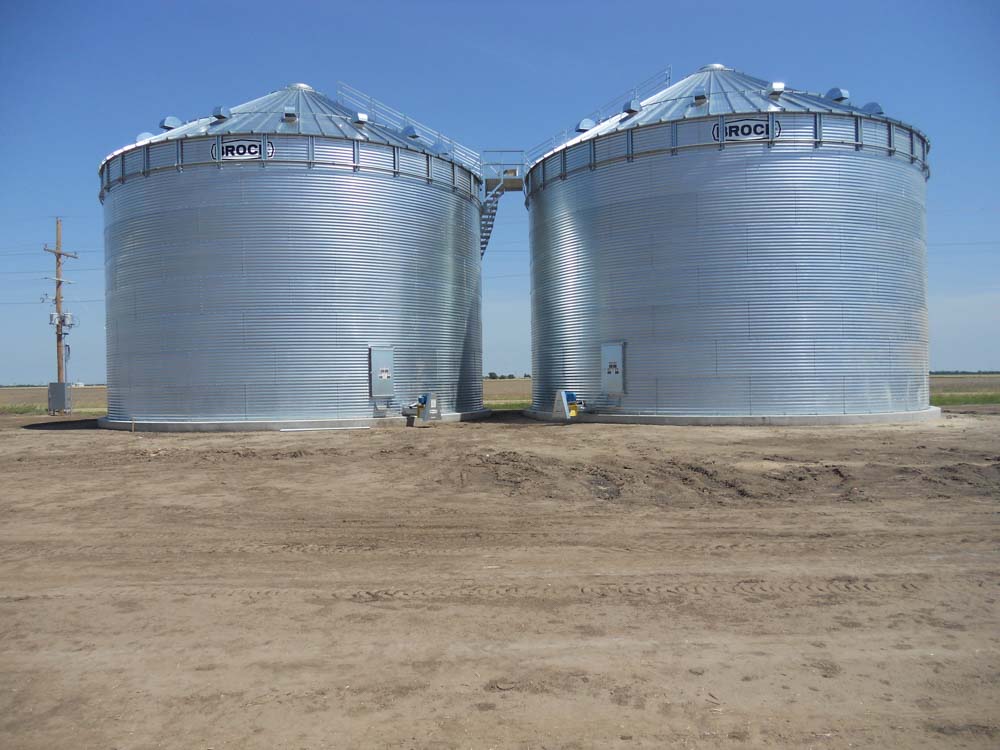 2 large metal grain bins next to a field