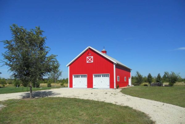 Red metal barn with two garage doors and a circle gravel drive