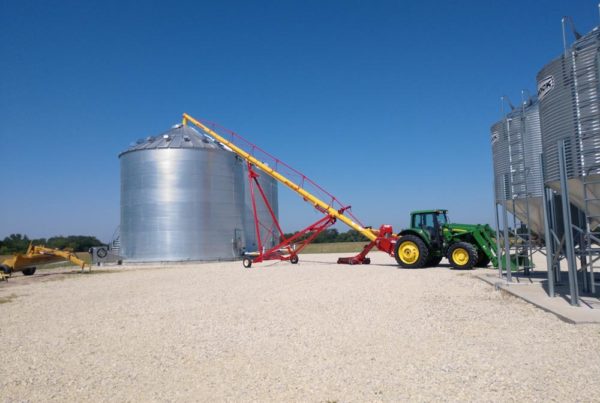 Tractor using auger to move grain into large metal grain bin