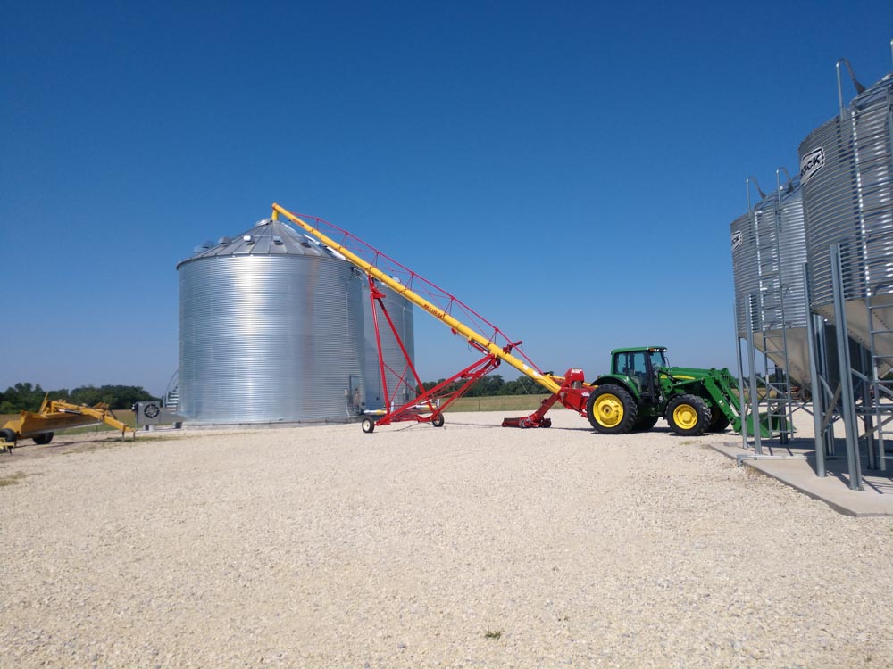 Tractor using auger to move grain into large metal grain bin